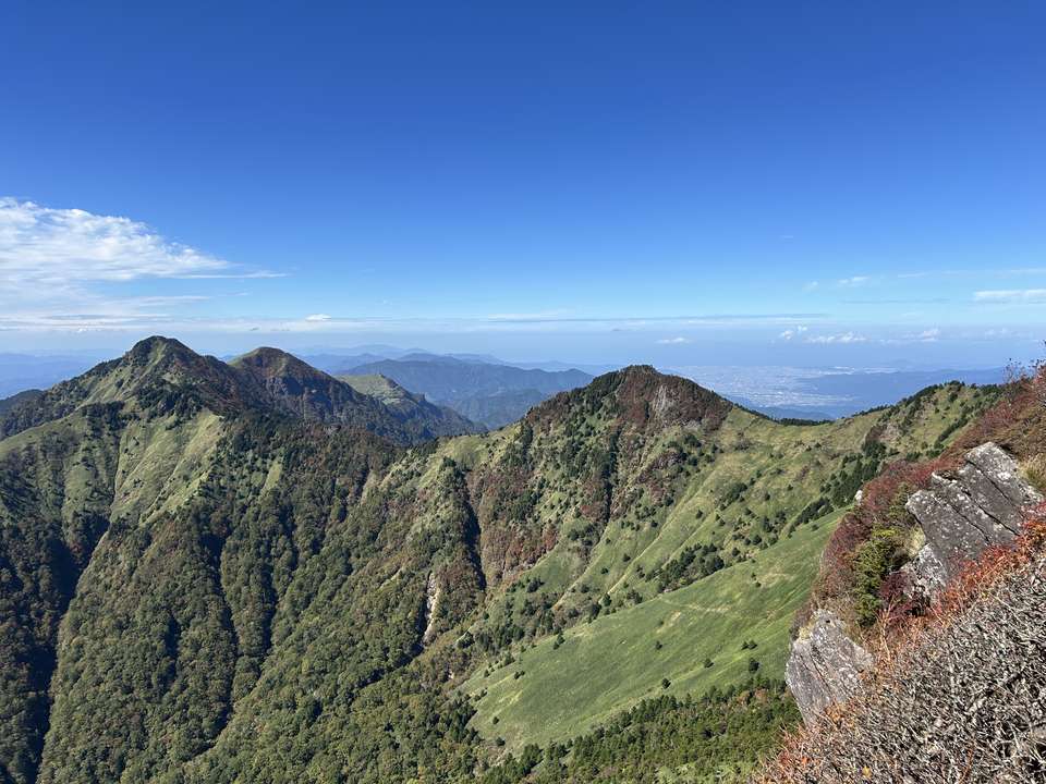 笹に覆われた稜線が連なり、遠くに平野と海が見える