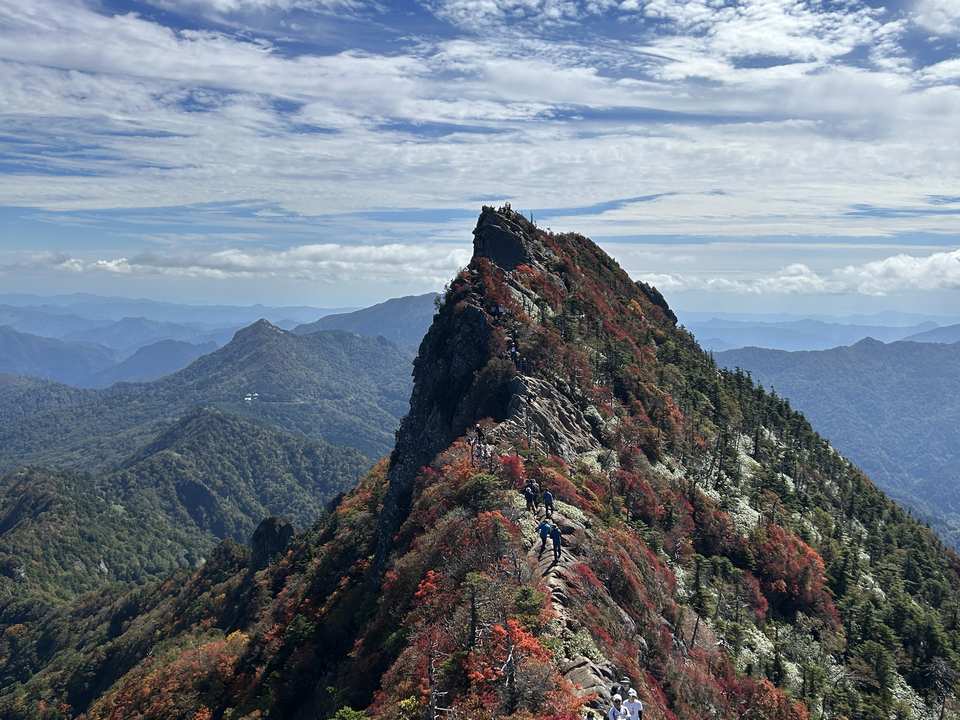弥山から見た天狗岳。紅葉の稜線を登山者が歩いている